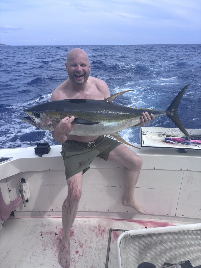 Grijnzende visser houdt een grote geelvintonijn omhoog in de kuip van de boot met de diepblauwe open oceaan achter hem bij Bonaire.