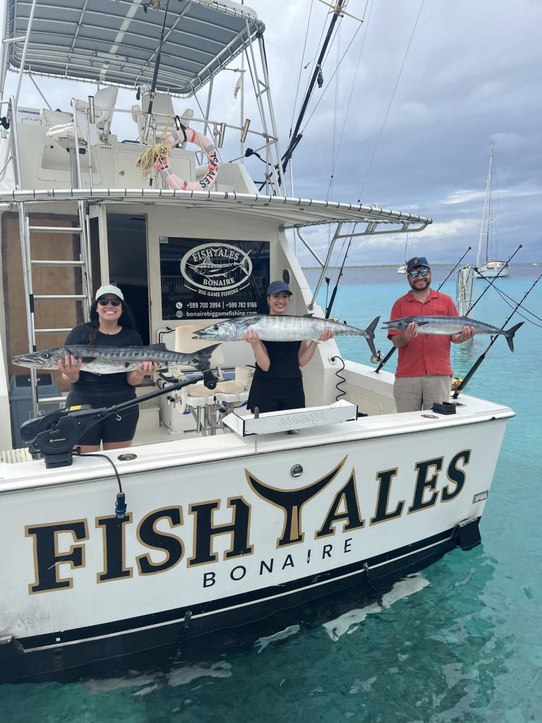 Drie vissers houden wahoo omhoog in de kuip van de Fish Tales Bonaire-sportvisser drijvend op helder turquoise Caribisch water.