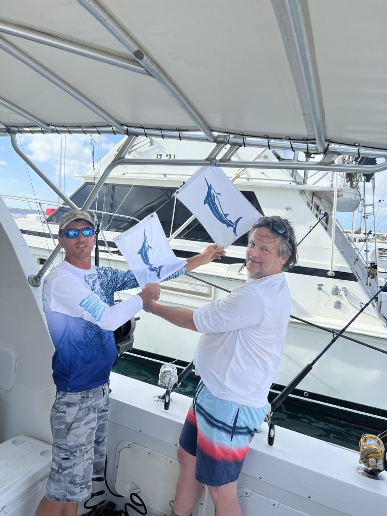 Kapitein en visser houden release-vlaggen voor blauwe marlijn omhoog aan boord van de Fishtales Bonaire-boot bij de marina na het vangen van een billfish.