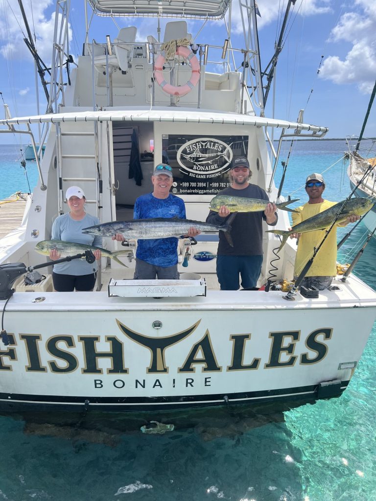 Vier mensen staan op de spiegel van de Fish Tales Bonaire-sportvisser met wahoo en mahi-mahi boven helder turquoise water.