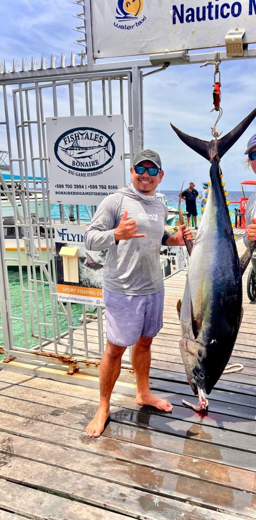 Fishtales Bonaire crew member Orlando holding a big yellowfin tuna at the dock by the Fishtales sign, Nautico Marina, Bonaire