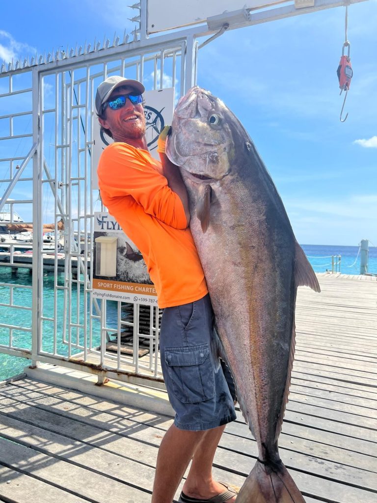 Fishtales Bonaire mate Vincent in an orange shirt hoisting a giant amberjack on the dock in Kralendijk, Bonaire