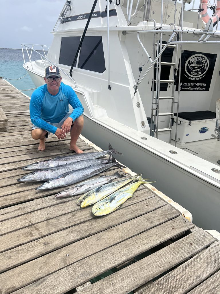 Visser knielt op de steiger van Bonaire naast een rij wahoo en gouden mahi-mahi die door de Fish Tales boot zijn uitgelegd.