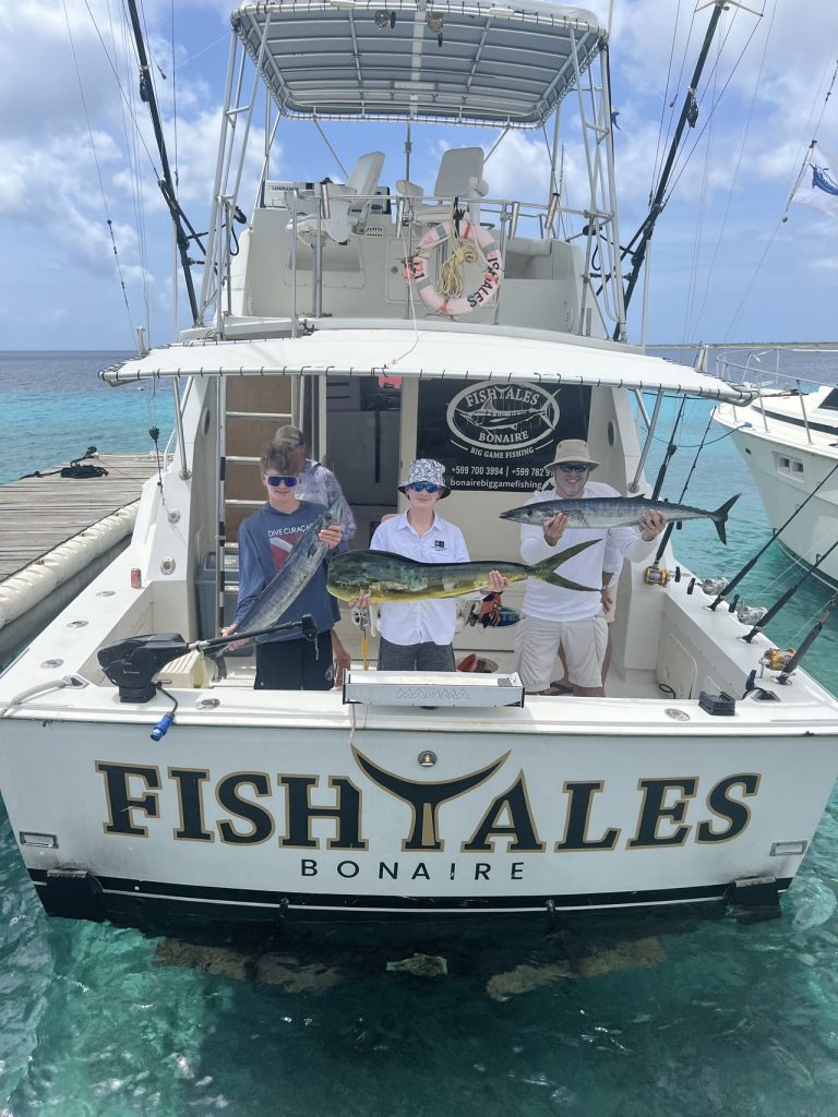 Jonge vissers en bemanning houden een mahi-mahi en een wahoo vast bij de achtersteven van de Fish Tales Bonaire boot in turquoise water