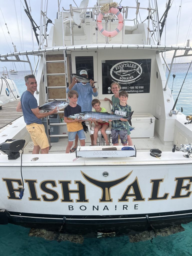 Een man en drie jonge jongens houden tonijn en wahoo vast op de spiegel van de Fish Tales Bonaire Bertram in helder Caribisch water.