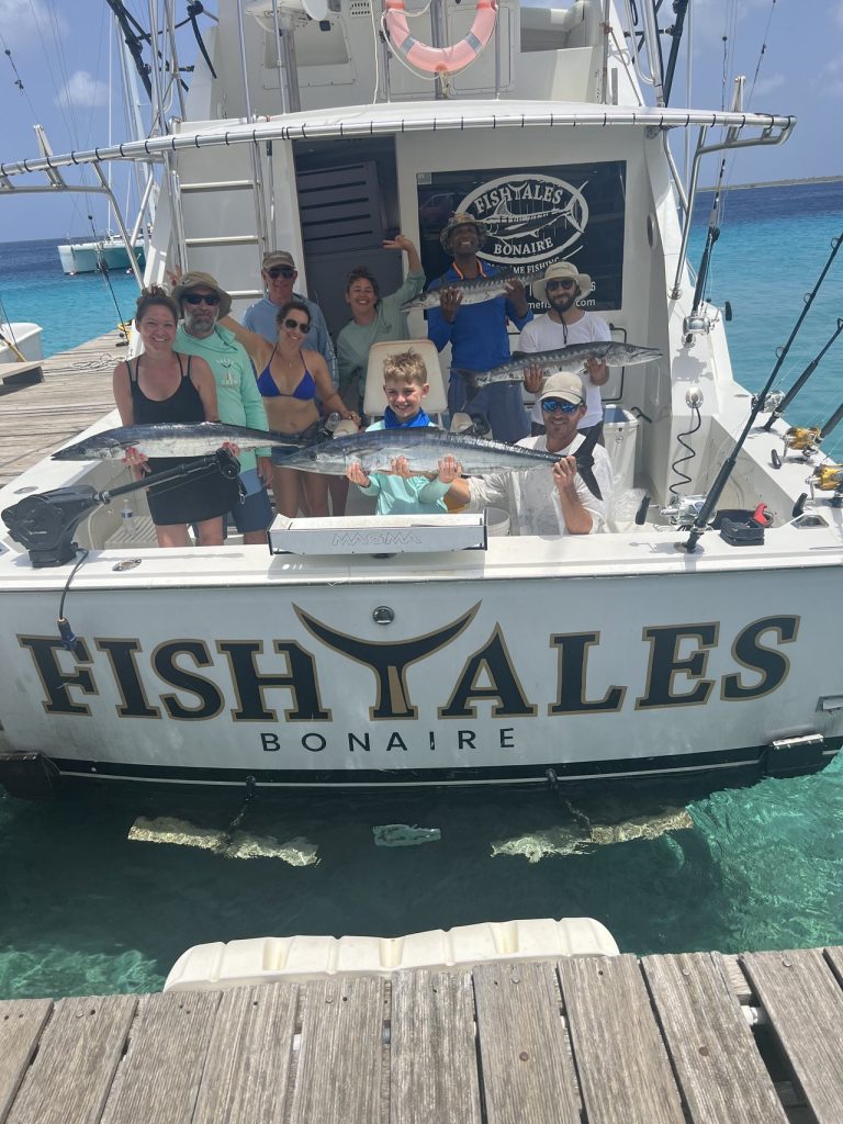 Een grote groep met kinderen op de Fish Tales Bonaire boot houdt wahoo en barracuda vast aan de steiger met de bemanning.
