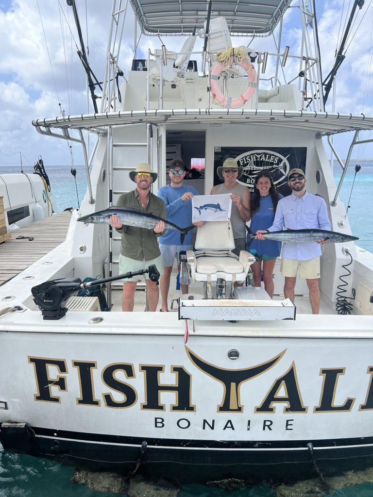 Vijf gasten houden twee wahoo en een billfish-releasecertificaat vast op het achterdek van de Fishtales Bonaire sportvisboot.