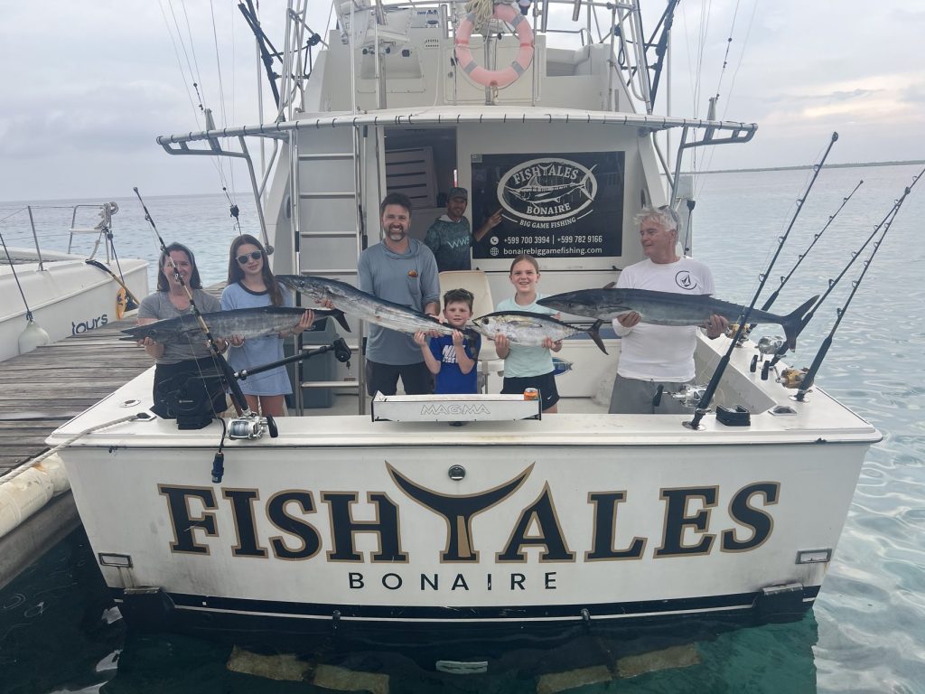 Gezinsgroep met wahoo bij de achtersteven van de FISH TALES Bonaire charterboot in de schemering in de jachthaven van Kralendijk na het vissen.