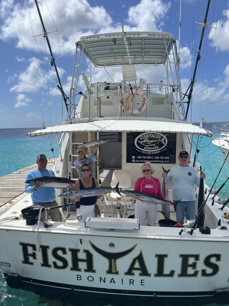 Vissers en familie houden wahoo vast op de achtersteven van de Fishtales Bonaire-vissersboot boven helder turquoise Caribisch water.