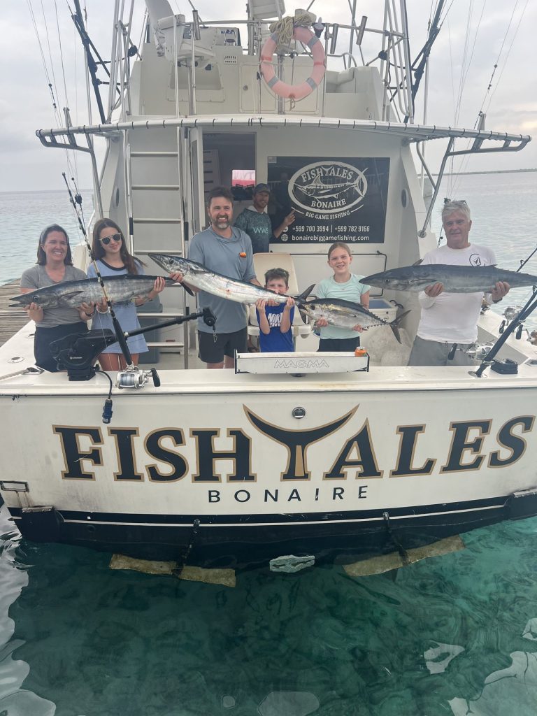 Gezin van zes op de steiger met wahoo en tonijn achter de FISH TALES Bonaire spiegel na een big game fishing charter in Kralendijk.