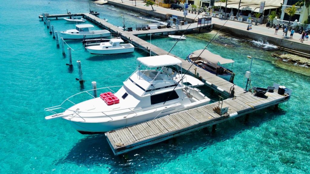Luchtfoto van de witte Fishtales Bertram sportvisboot afgemeerd aan een steiger in het turquoise water van Nautico Marina, Bonaire