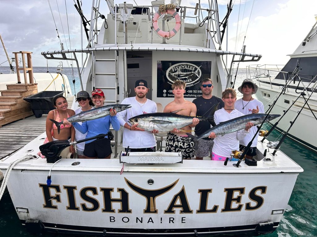 Acht lachende gasten op de achtersteven van de Fishtales-boot aan de steiger met meerdere tonijnen na een visreis op Bonaire
