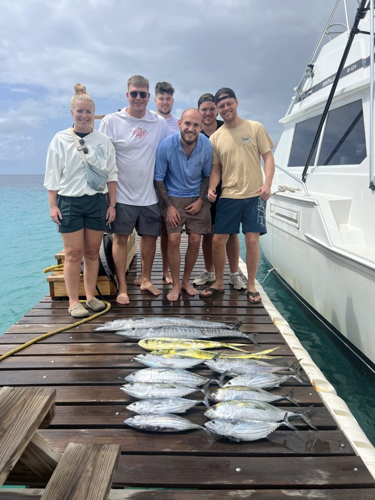 Zes sportvissers staan op de kade naast de charterboot met een rij tonijn, mahi-mahi en wahoo voor hen uitgestald.