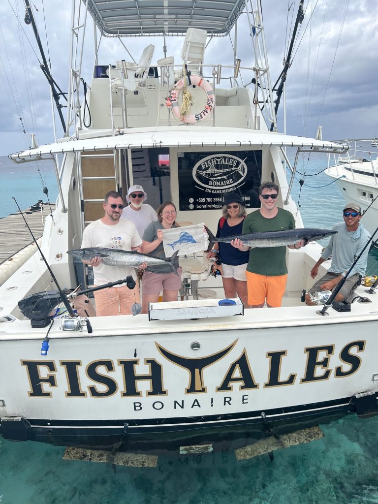 Zes vissers en bemanning houden meerdere wahoo en een marlijnvlag vast bij de achtersteven van de Fish Tales Bonaire charterboot