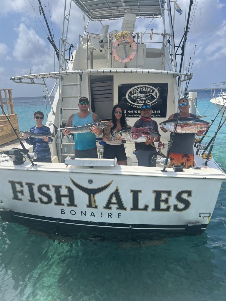 Vijf sportvissers houden wahoo en tonijn vast op het achterdek van de Fishtales Bonaire sportvisser in helder turquoise water.