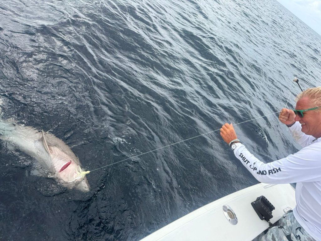 Visser in een Shut Up And Fish-shirt haalt een big game vis naar de zijkant van de boot boven kalm blauw water bij Bonaire.