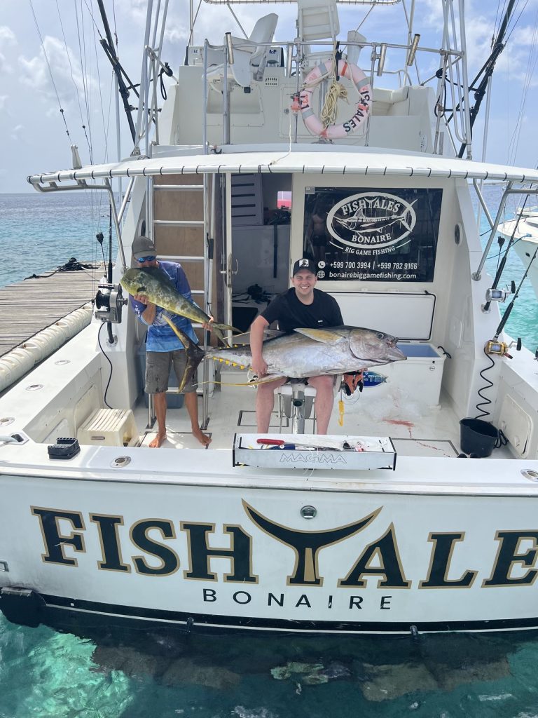 Two anglers on the Fish Tales Bonaire boat holding a mahi-mahi and a heavy amberjack at the stern in turquoise water