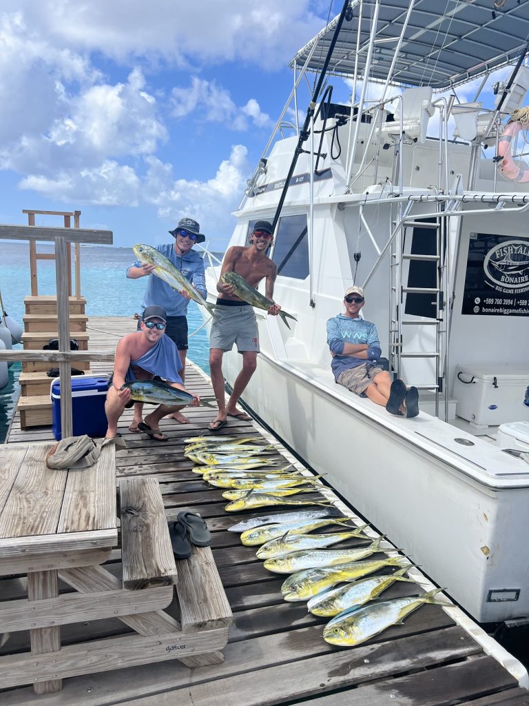 Bemanning op de steiger naast de Fishtales-boot toont felle mahi-mahi dorado, met een lange rij vissen uitgelegd op de planken.
