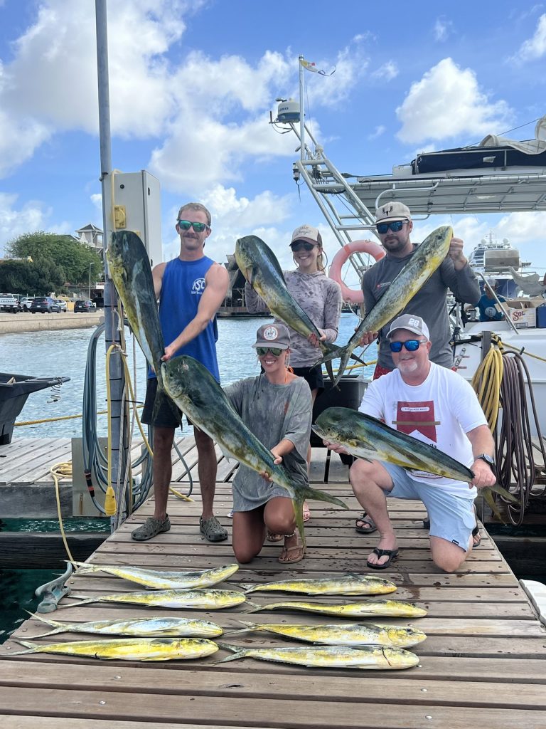 Groep van vijf vissers op een steiger van Bonaire met fel groen-gele mahi-mahi dorado, met meer vissen voor hun voeten uitgelegd.