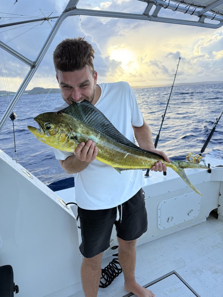 Young man on the boat playfully biting a freshly caught golden-green mahi-mahi dorado at sunset off Bonaire.