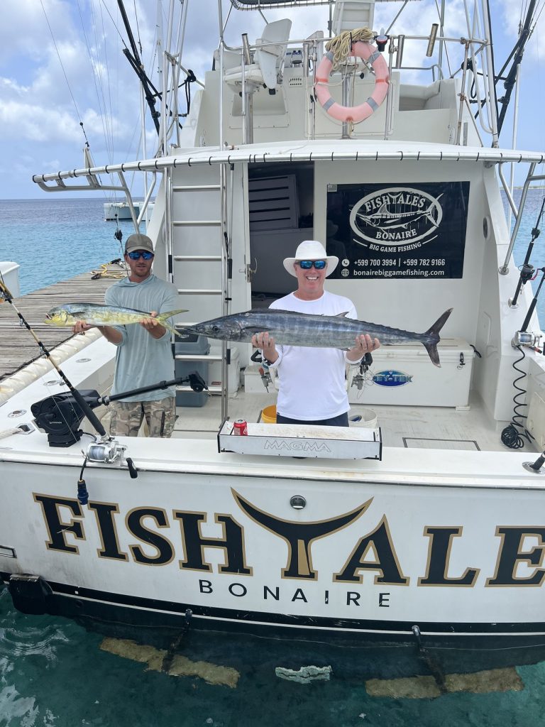 Twee vissers bij de achtersteven van de FISH TALES Bonaire boot met een mahi-mahi en een wahoo na een big game fishing charter op Bonaire.