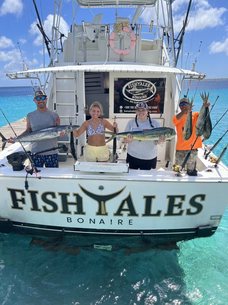Vier gasten aan de achtersteven van de FISH TALES Bonaire-boot met mahi-mahi en wahoo boven turquoise water na een vischarter.