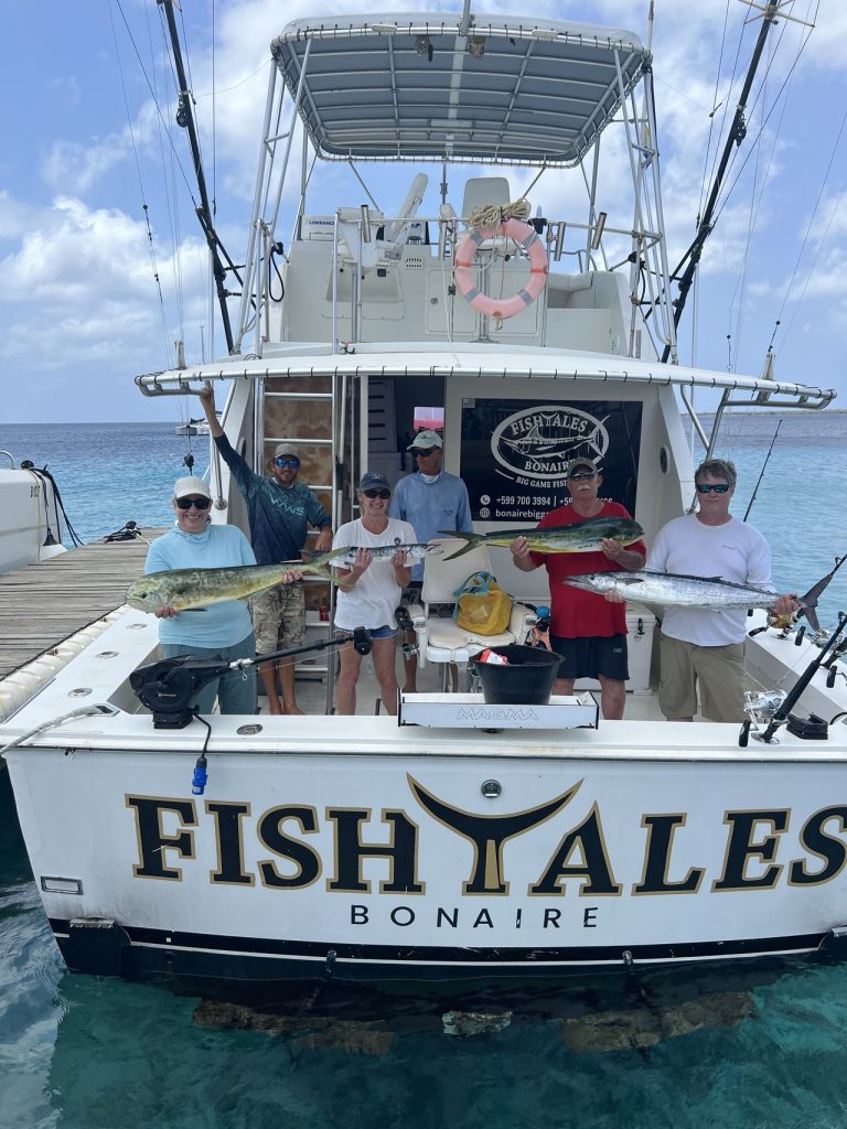 Zes vissers en bemanning houden mahi-mahi en wahoo vast over de achtersteven van de Fish Tales Bonaire sportvisboot in helder water