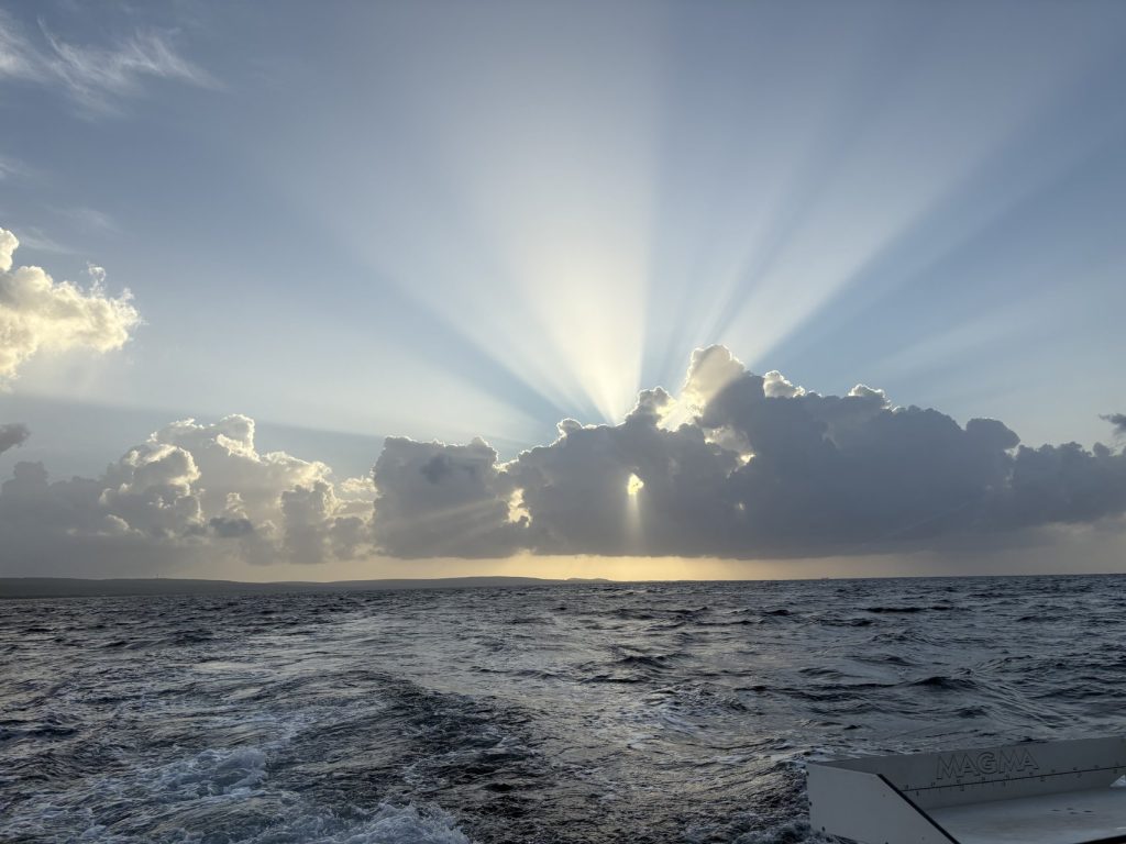 Dramatische zonnestralen breken door de wolken boven de open zee achter het kielzog van de Fishtales-boot voor Bonaire tijdens het gouden uur