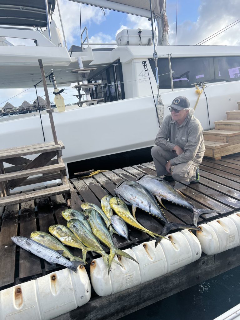 Visser geknield naast een rij tonijn, mahi-mahi en wahoo uitgelegd op de steiger naast een afgemeerde boot op Bonaire.