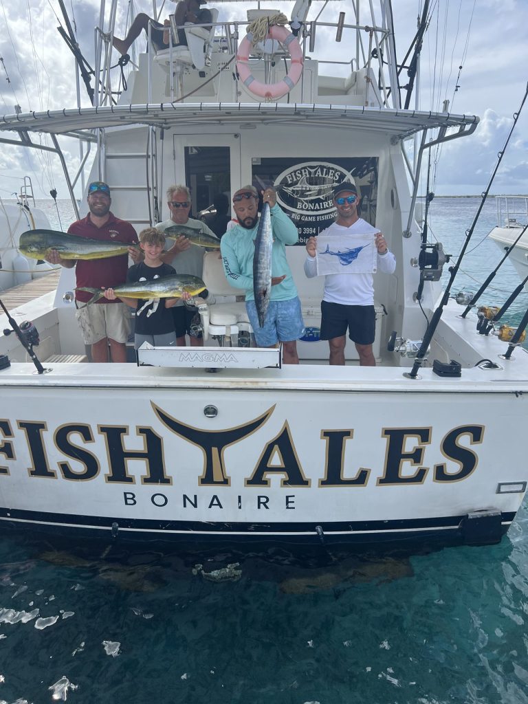 Vierkoppige familie op de Fishtales Bertram-sportvisser op Bonaire met een wahoo en mahi-mahi, spiegel met opschrift FISH TALES BONAIRE.