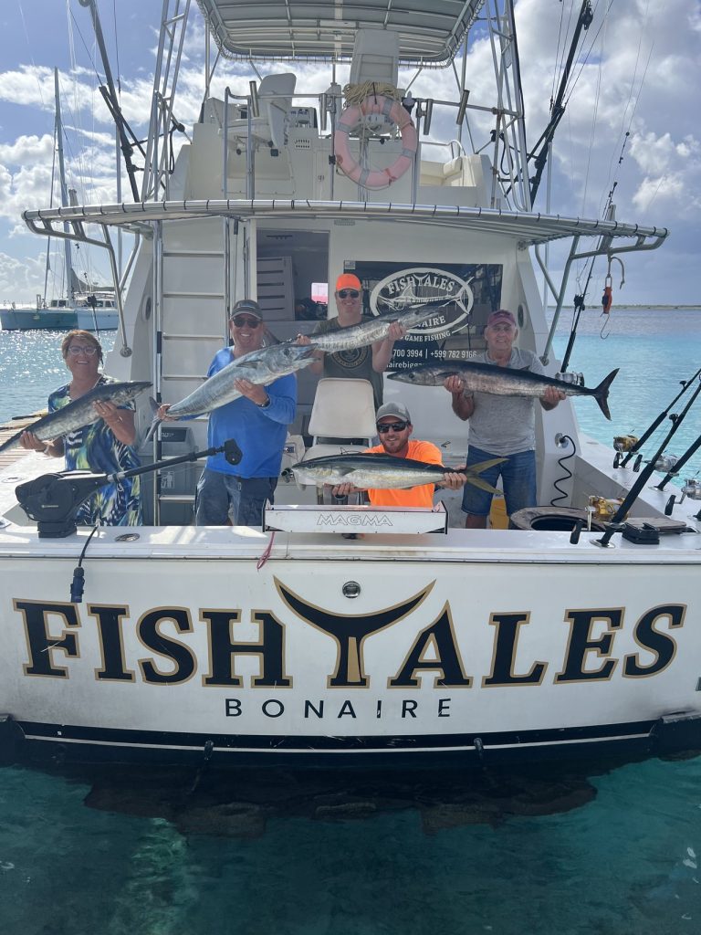 Vijf vissers op de Fishtales Bonaire-sportvisser met meerdere wahoo en een tonijn boven de spiegel met opschrift FISH TALES BONAIRE.