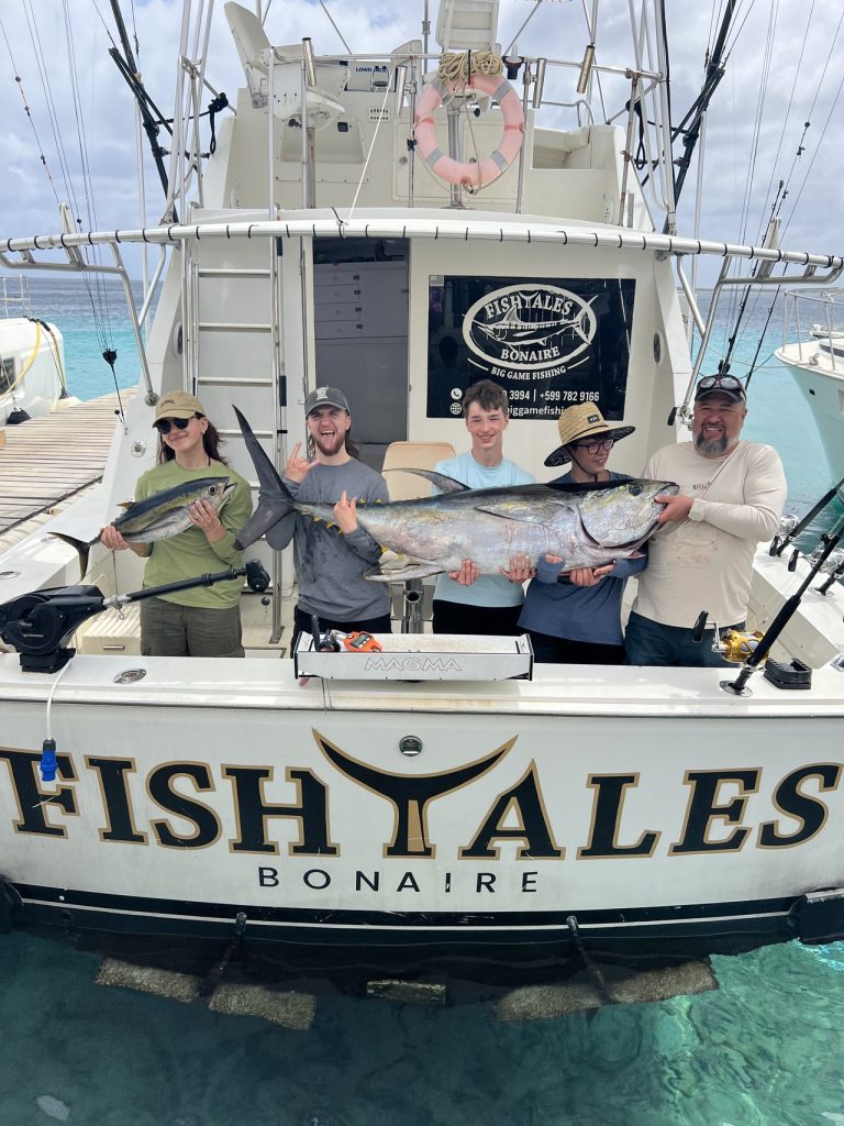 Vijf vissers aan de spiegel van de sportvisser Fish Tales Bonaire houden een wahoo en een grote geelvintonijn vast boven helder water.