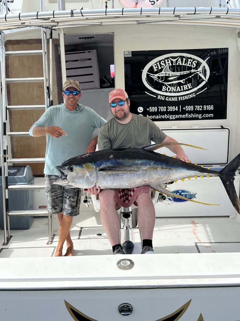 Twee vissers houden een grote geelvintonijn vast op het dek van de Fishtales Bonaire big game fishing-boot bij de steiger.