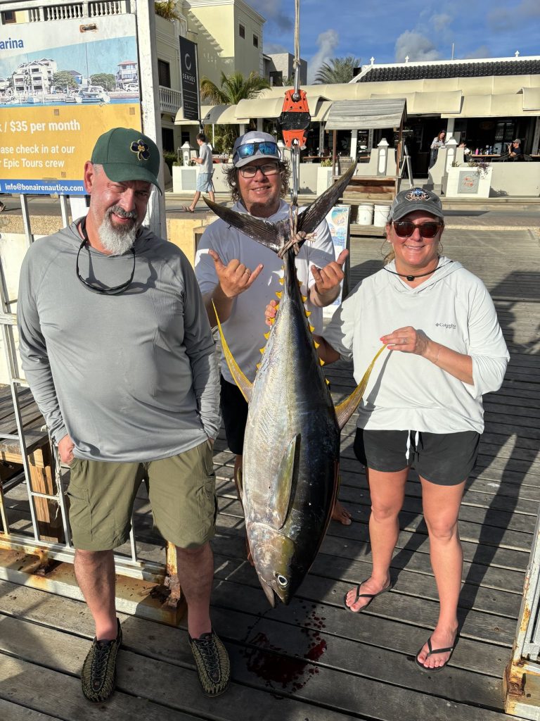 Drie gasten op de haventrap houden een grote geelvintonijn en de lijn vast na een vistocht op Bonaire.