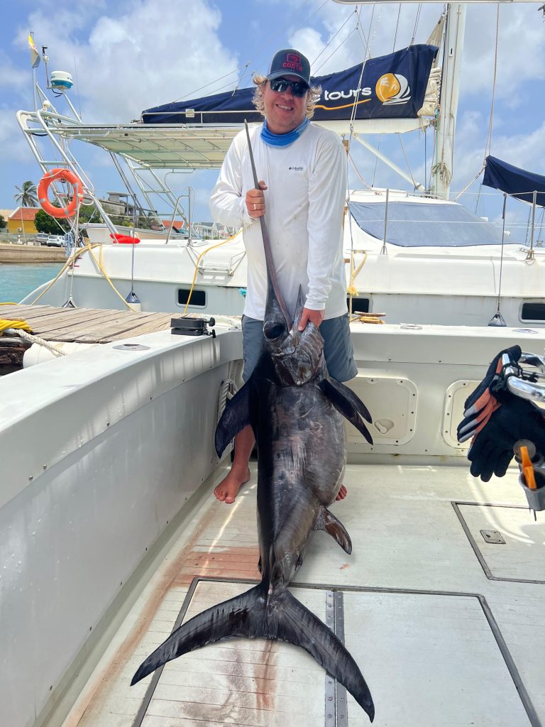 Angler hält einen Schwertfisch aufrecht am Schwert an Bord der Fishtales